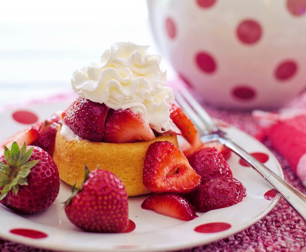 Das Bild zeigt einen kleinen Kuchen mit Erdbeeren und Sahne.